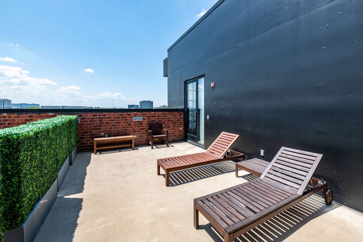Une terrasse sur le toit, dotée de chaises longues en bois, d’une table et d’une porte vitrée donnant accès à un espace intérieur.