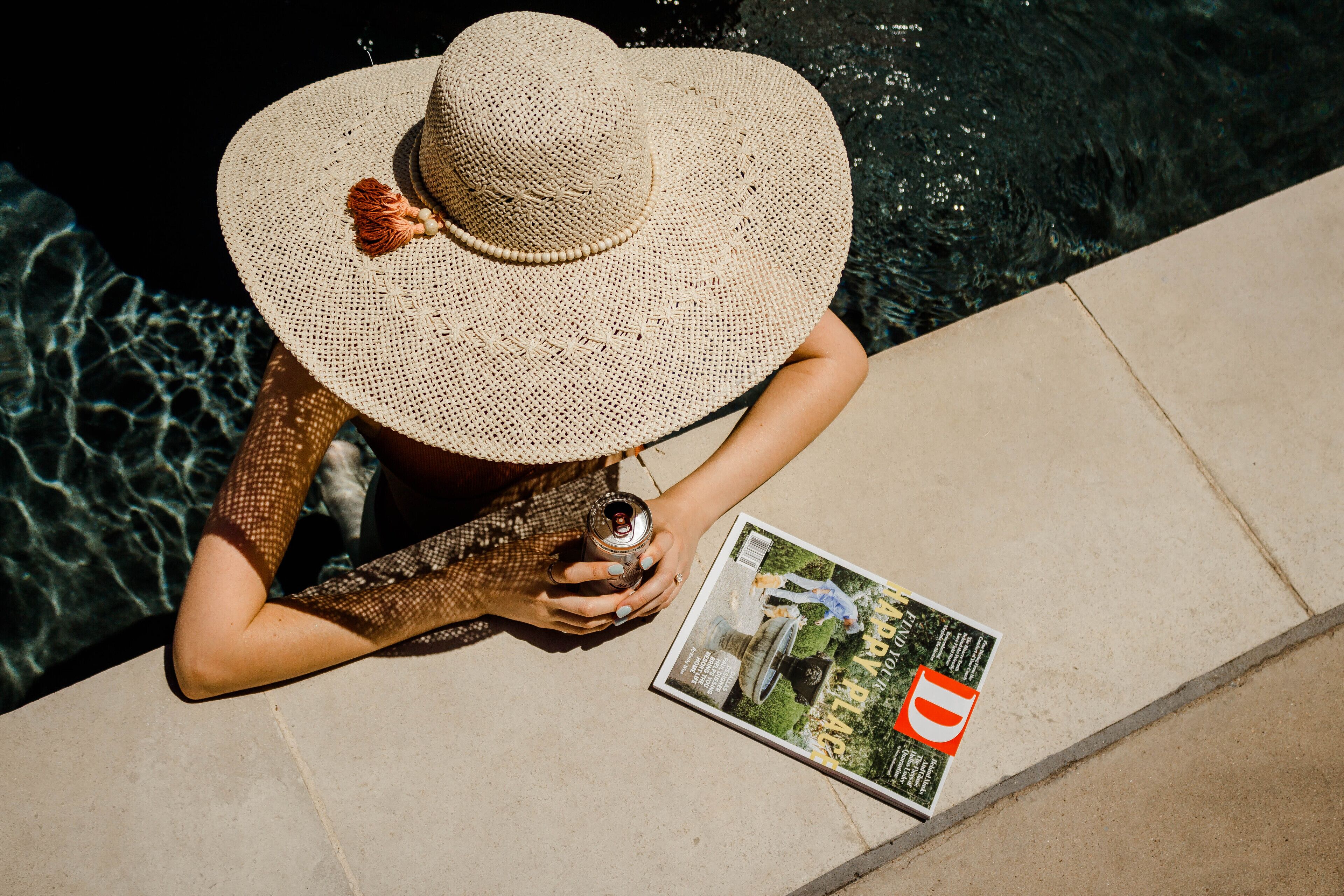 Una persona sentada junto a una piscina con una revista.