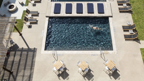 An aerial view of a pool area with lounge chairs, a diving board, and a swimmer.