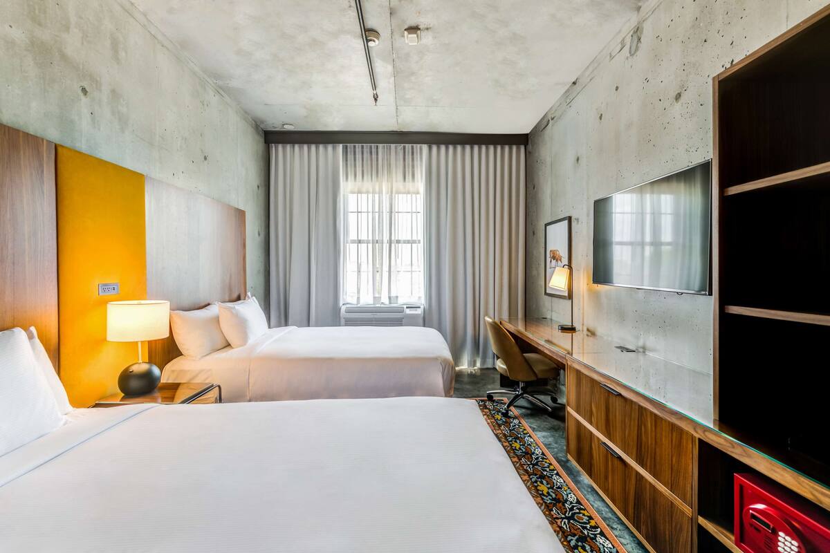 Une chambre d’hôtel avec deux lits, un bureau avec une chaise, une télévision et une fenêtre avec des rideaux.