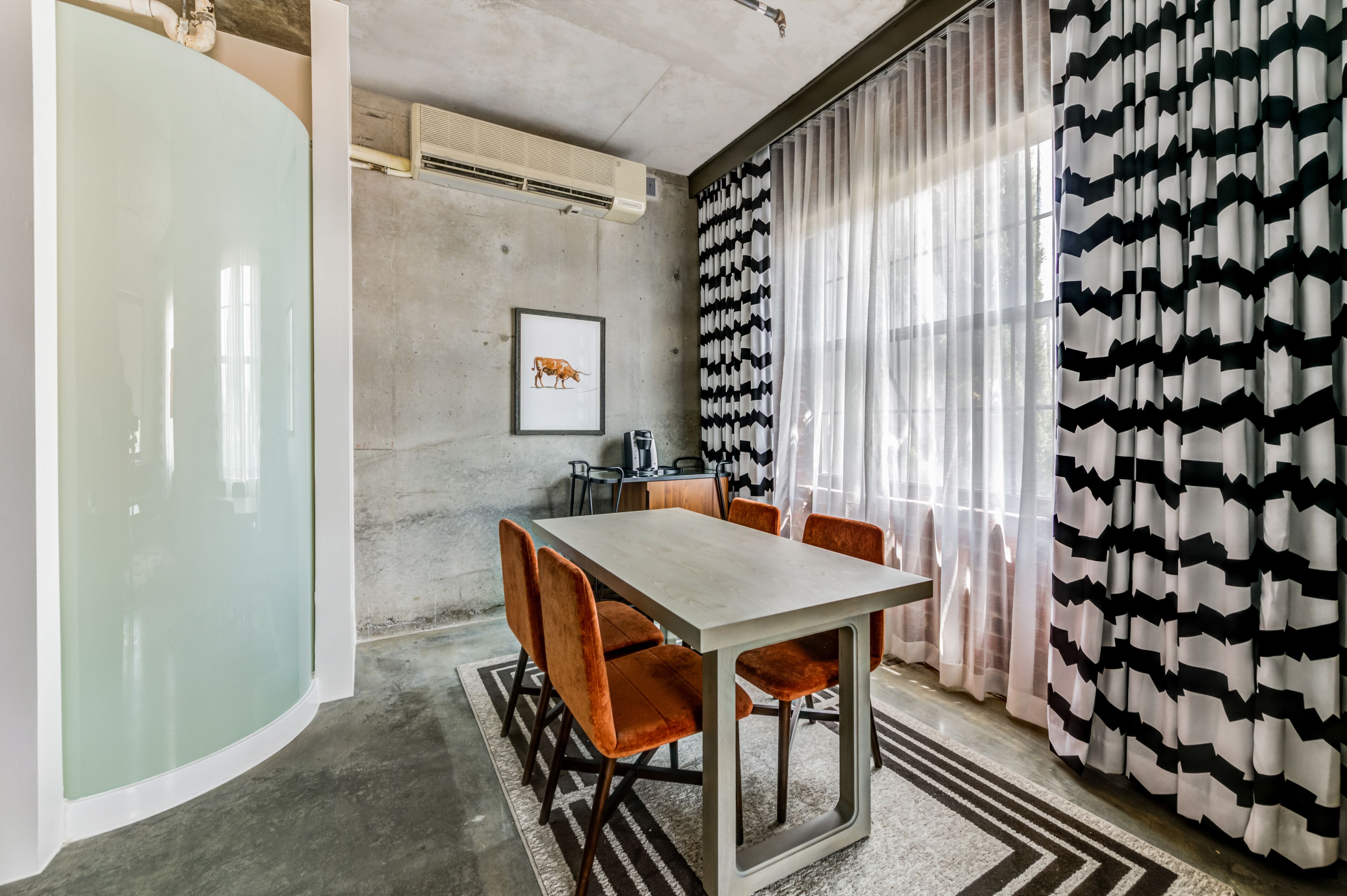 A modern dining area with a rectangular table, orange upholstered chairs, and a framed picture on the wall.