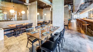 A spacious restaurant with high ceilings, exposed ductwork, and a long communal dining table set for a meal.