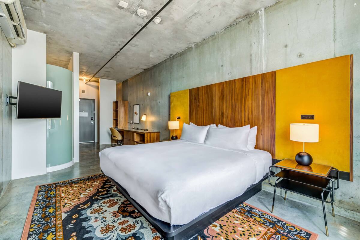 Une chambre d’hôtel moderne dotée d’un grand lit, d’un téléviseur à écran plat, d’un mur décoratif en bois et d’un tapis à motifs.