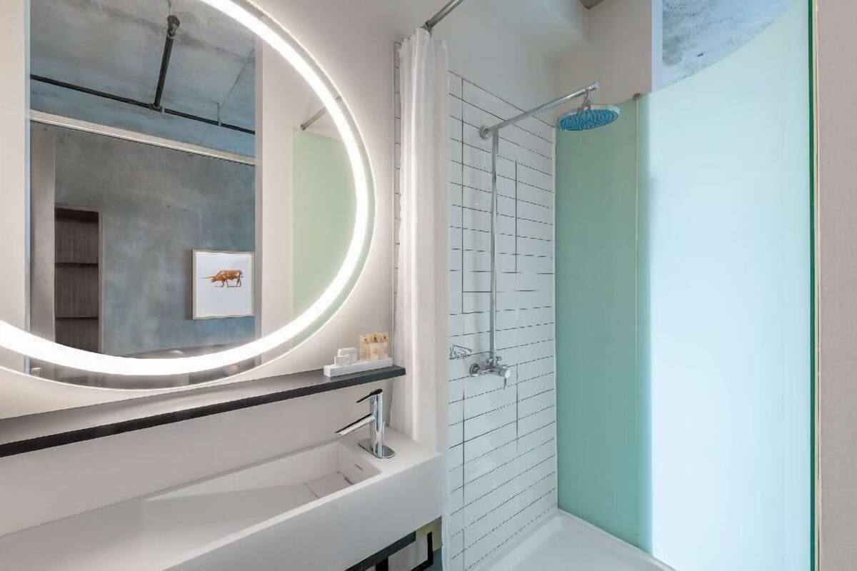 A modern bathroom with a round mirror, a shower, and a sink.