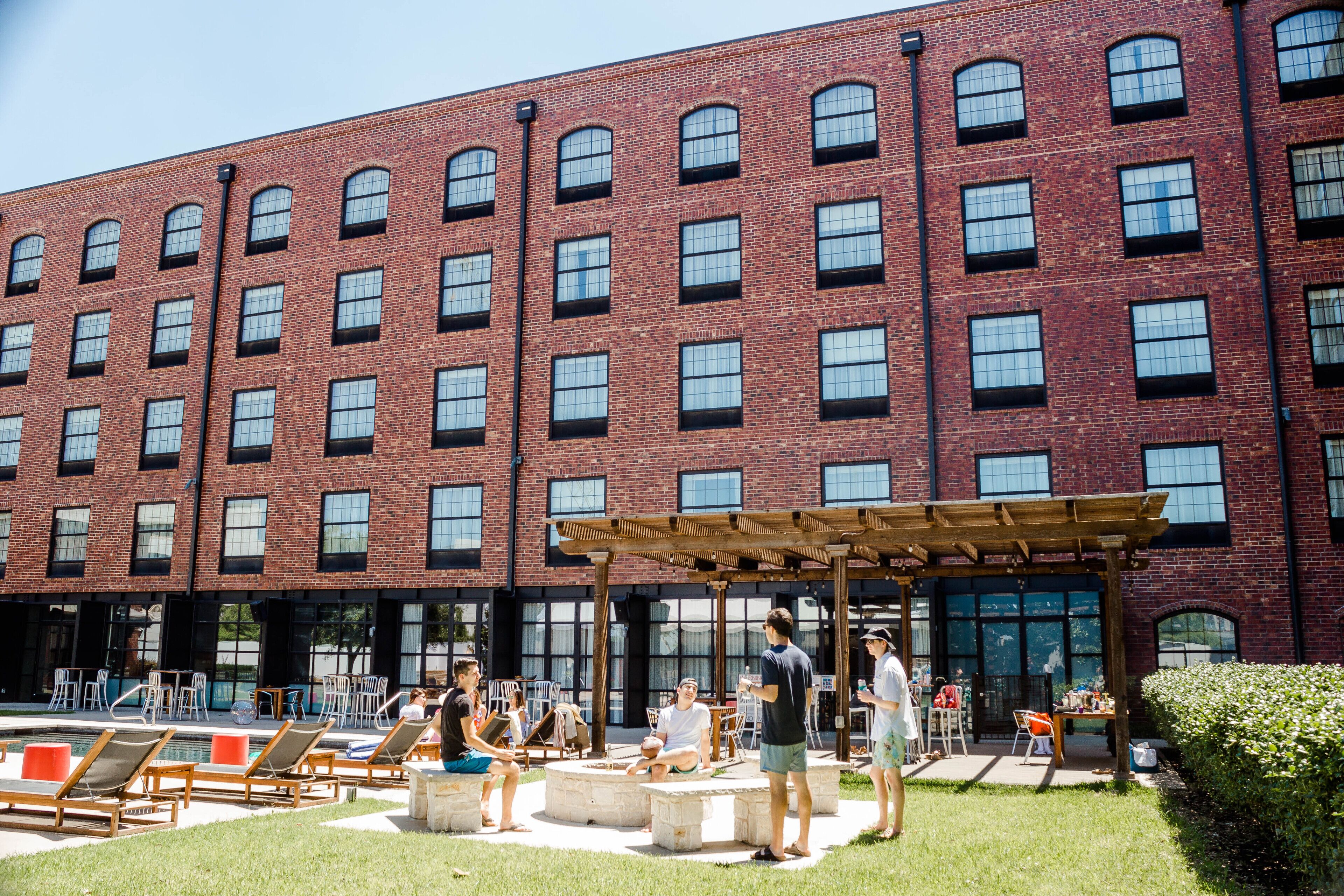 A brick building with multiple windows and a covered outdoor seating area with chairs and tables.