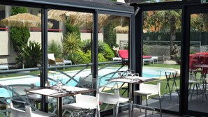 An outdoor dining area with tables and chairs, a pool, and a view of the surrounding garden.