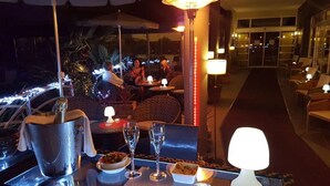 A bar area with a bottle of champagne, glasses, and a bowl of snacks. There are tables and chairs, and a person is visible in the background.