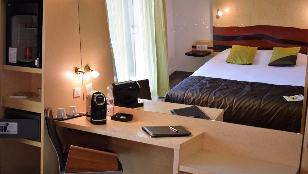 A hotel room with a bed, a desk with a laptop, a coffee maker, and a chair.
