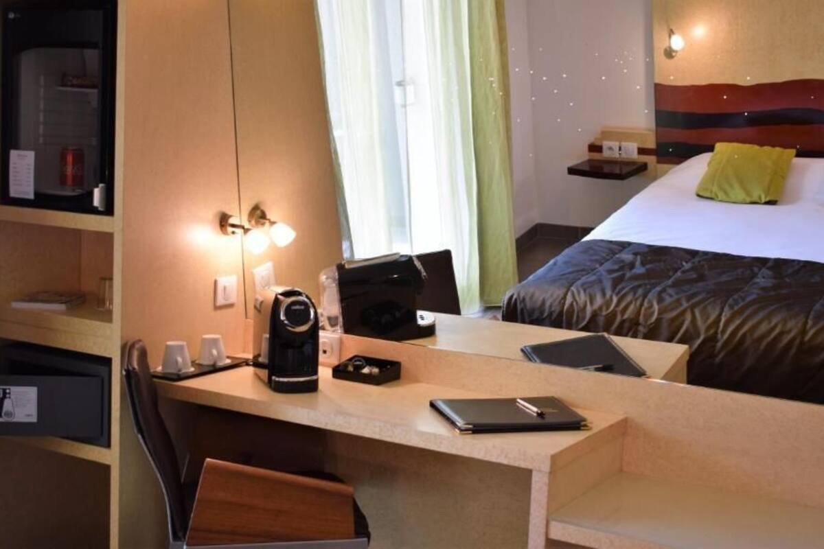 A hotel room with a bed, a desk with a laptop, a coffee maker, and a chair.