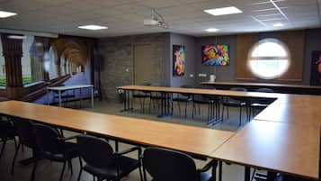 A conference room with long tables and chairs, a projector, and a stone wall.