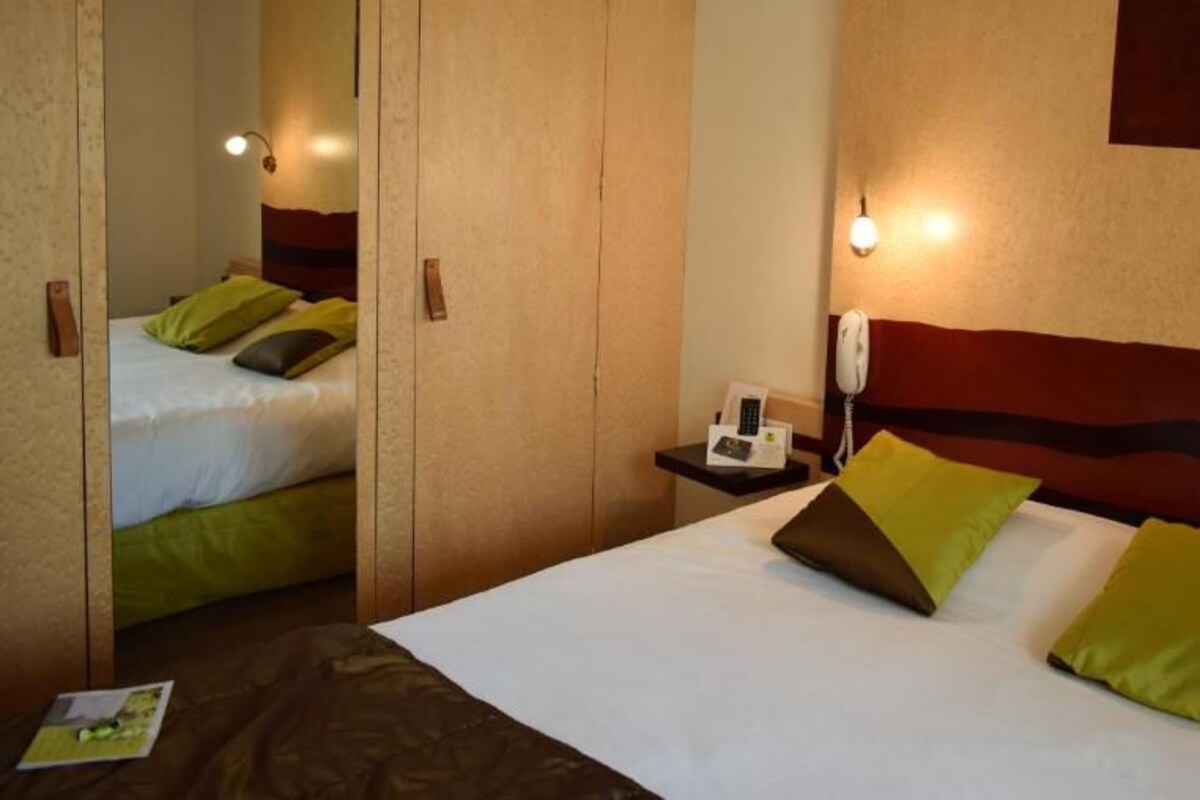 Una habitación de hotel con cama, mesita de noche, lámpara y espejo.