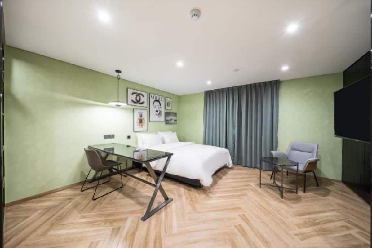 A hotel room with a bed, a glass table with chairs, a flat-screen TV, and a window with curtains.