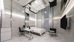 Une chambre d’hôtel moderne dotée d’un grand lit, d’un bureau avec une chaise, d’un téléviseur fixé au mur et d’un grand miroir.