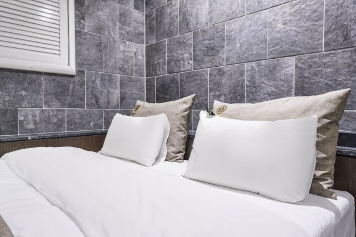 Une chambre d’hôtel avec un lit, du linge de lit blanc et des carreaux de marbre gris sur les murs.