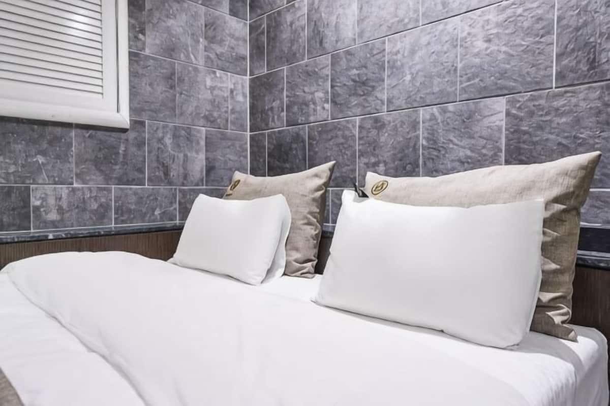 A hotel room with a bed, white bedding, and grey marble tiles on the walls.