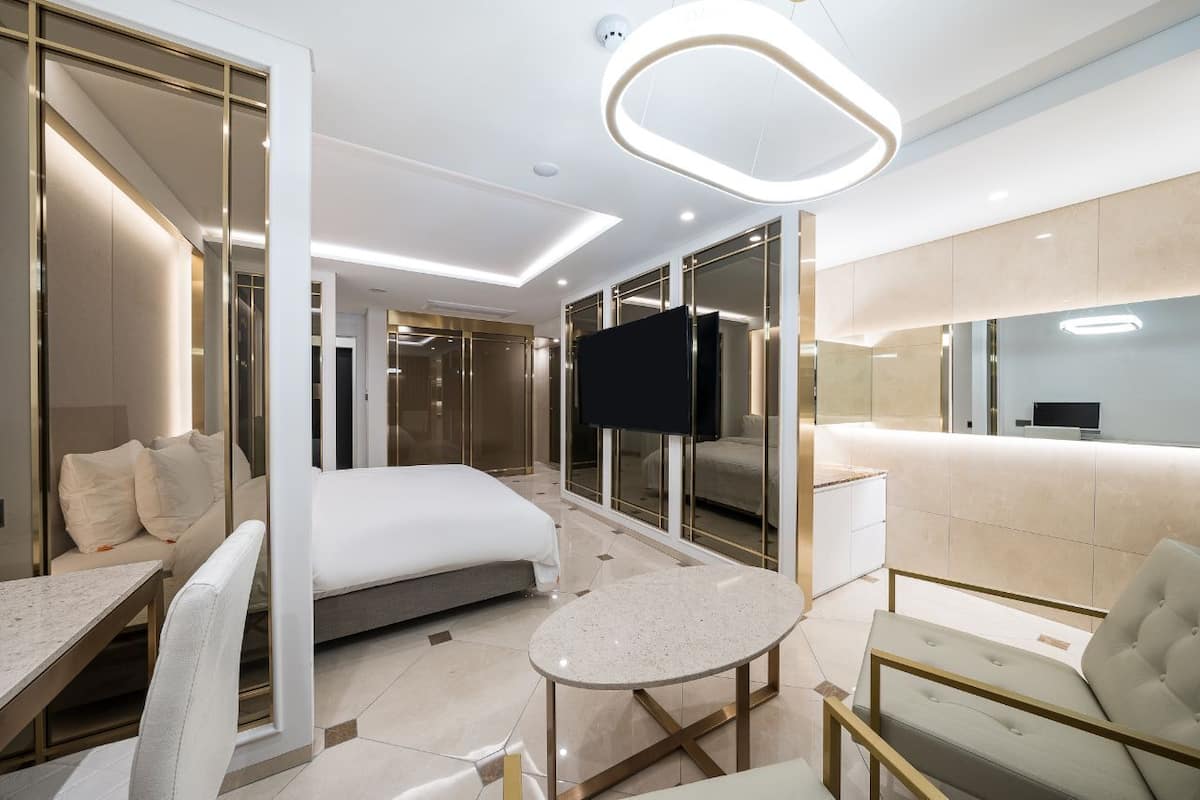 A modern hotel room with a bed, a TV, a seating area, and a large mirror.