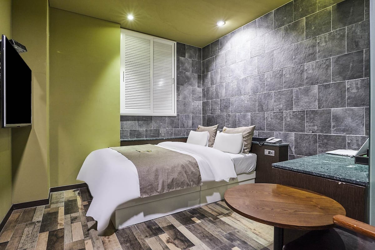A modern bathroom with a bed, a wooden floor, a round wooden table, and a shower area.