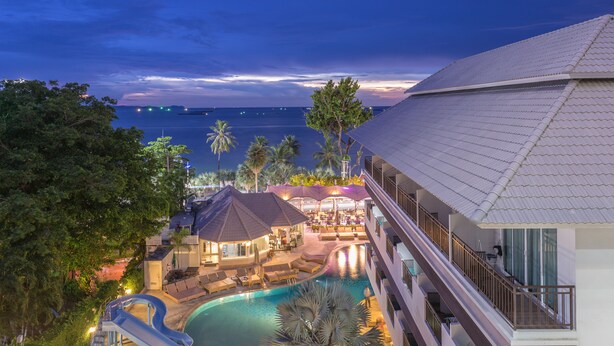 Un resort con piscina, zonas de descanso y vista al océano al anochecer.