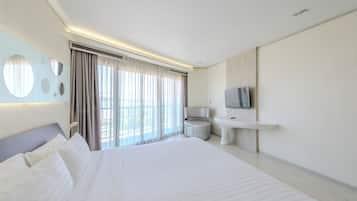 A modern hotel room with a large bed, a round mirror, a television, a round table, and a view of the outdoors.