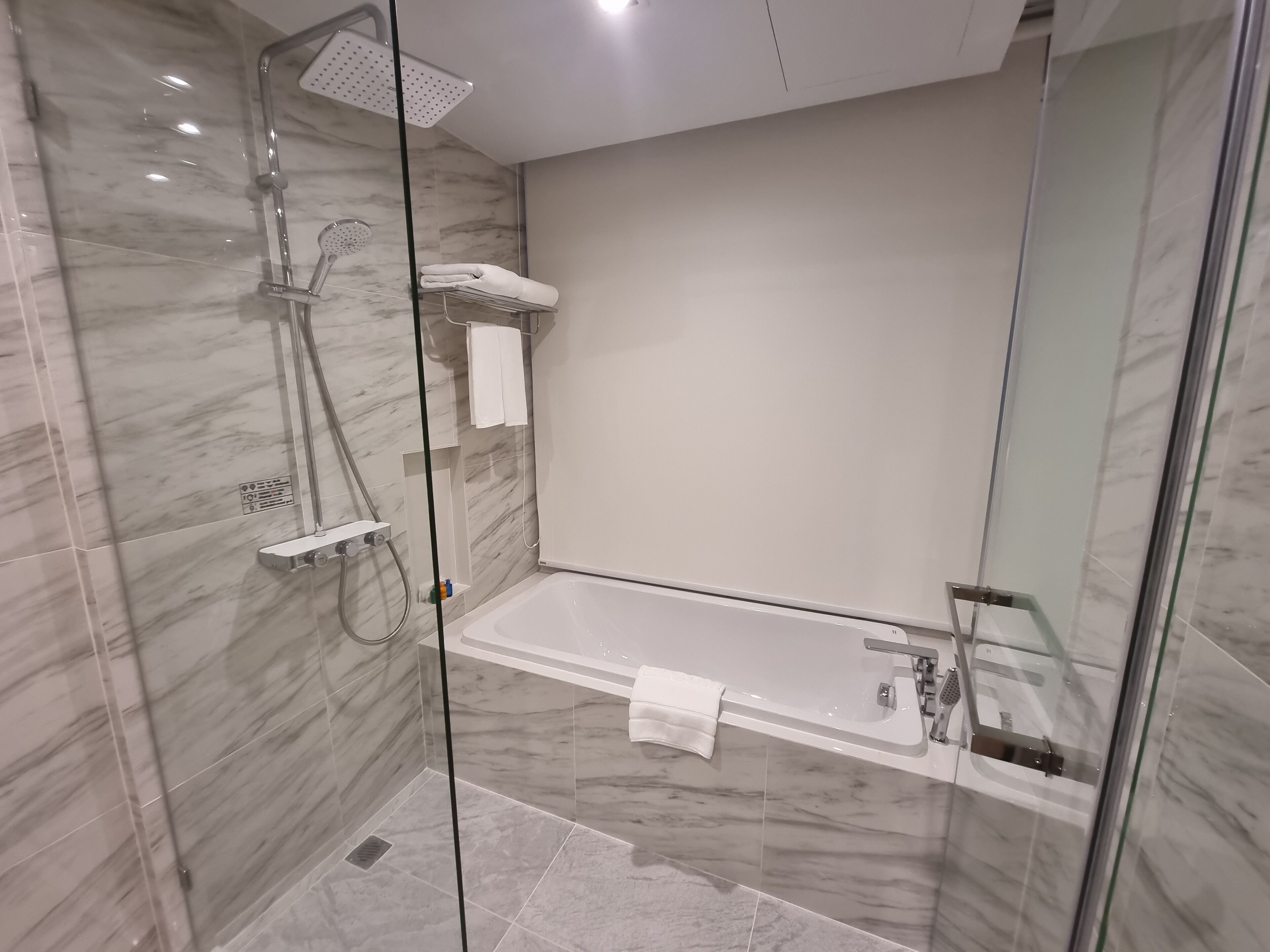 A modern bathroom with a glass-enclosed shower, a built-in bathtub, and marble walls.