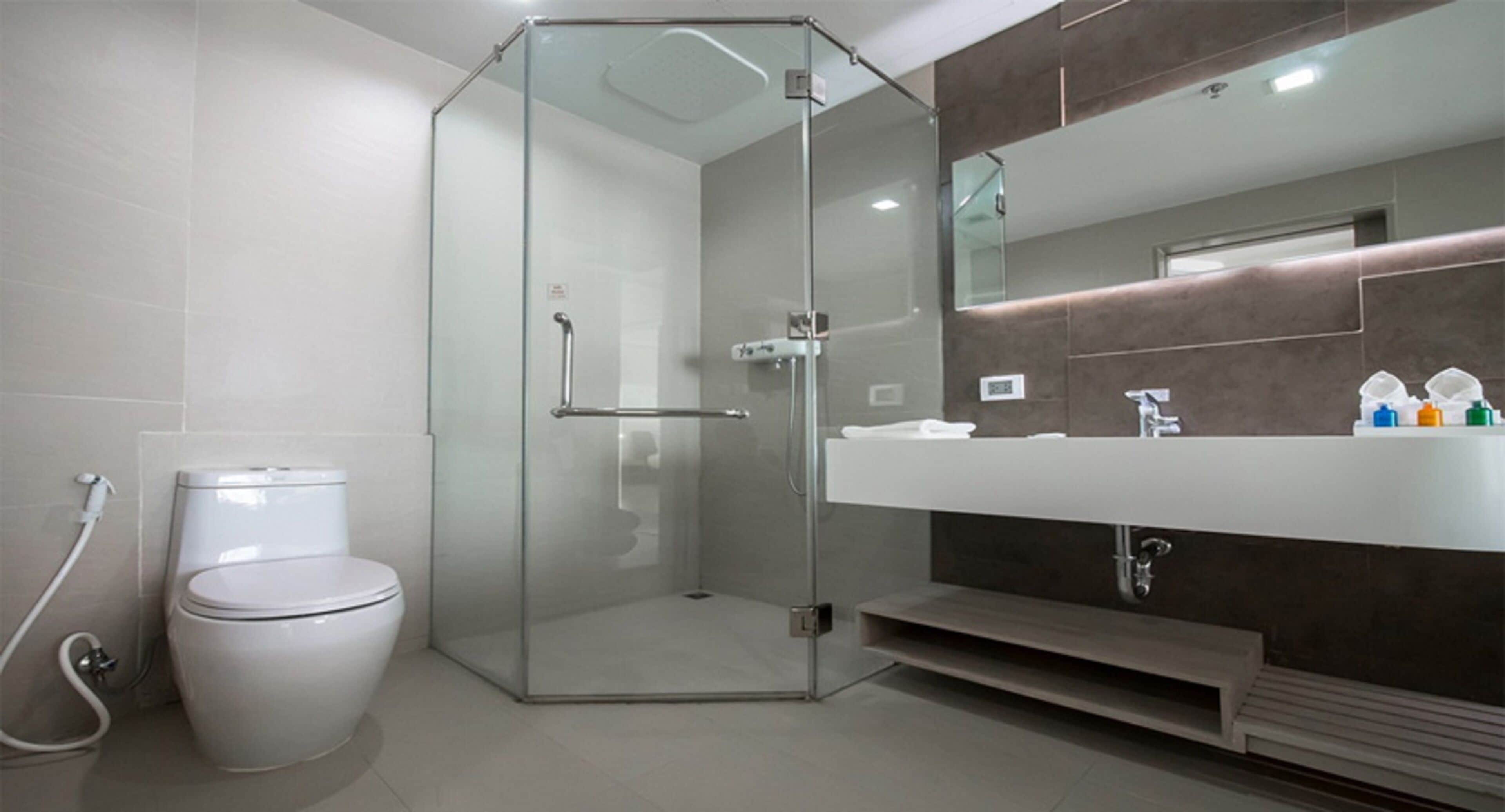 A modern bathroom with a glass-enclosed shower, a white toilet, and a large mirror above a white sink with a dark countertop.