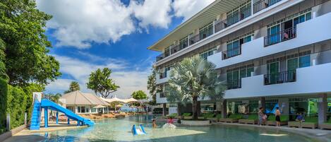 A hotel pool area with a blue slide, lounge chairs, and a building with balconies.