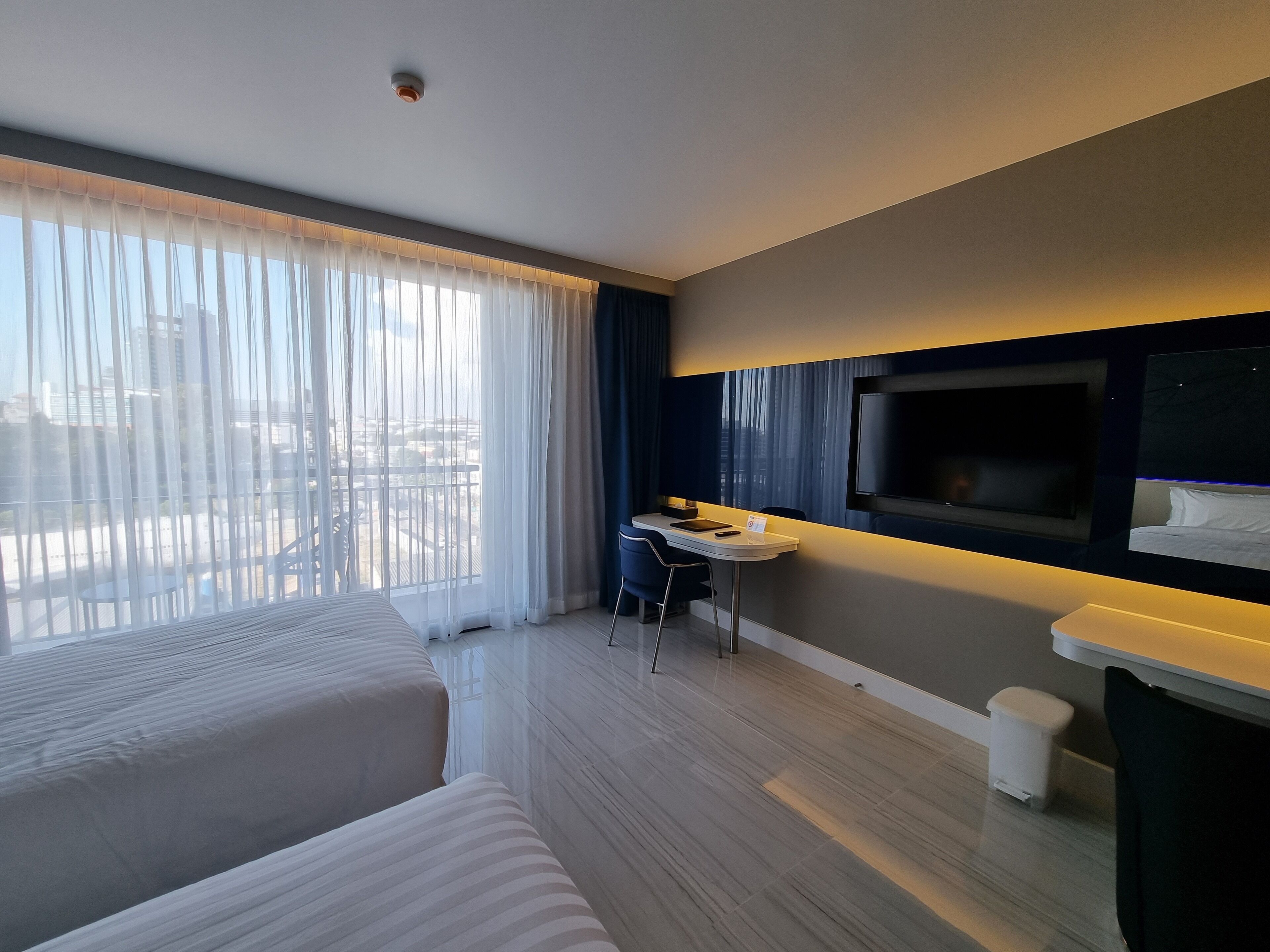 A hotel room with a bed, a desk, a TV, and a view of the city.
