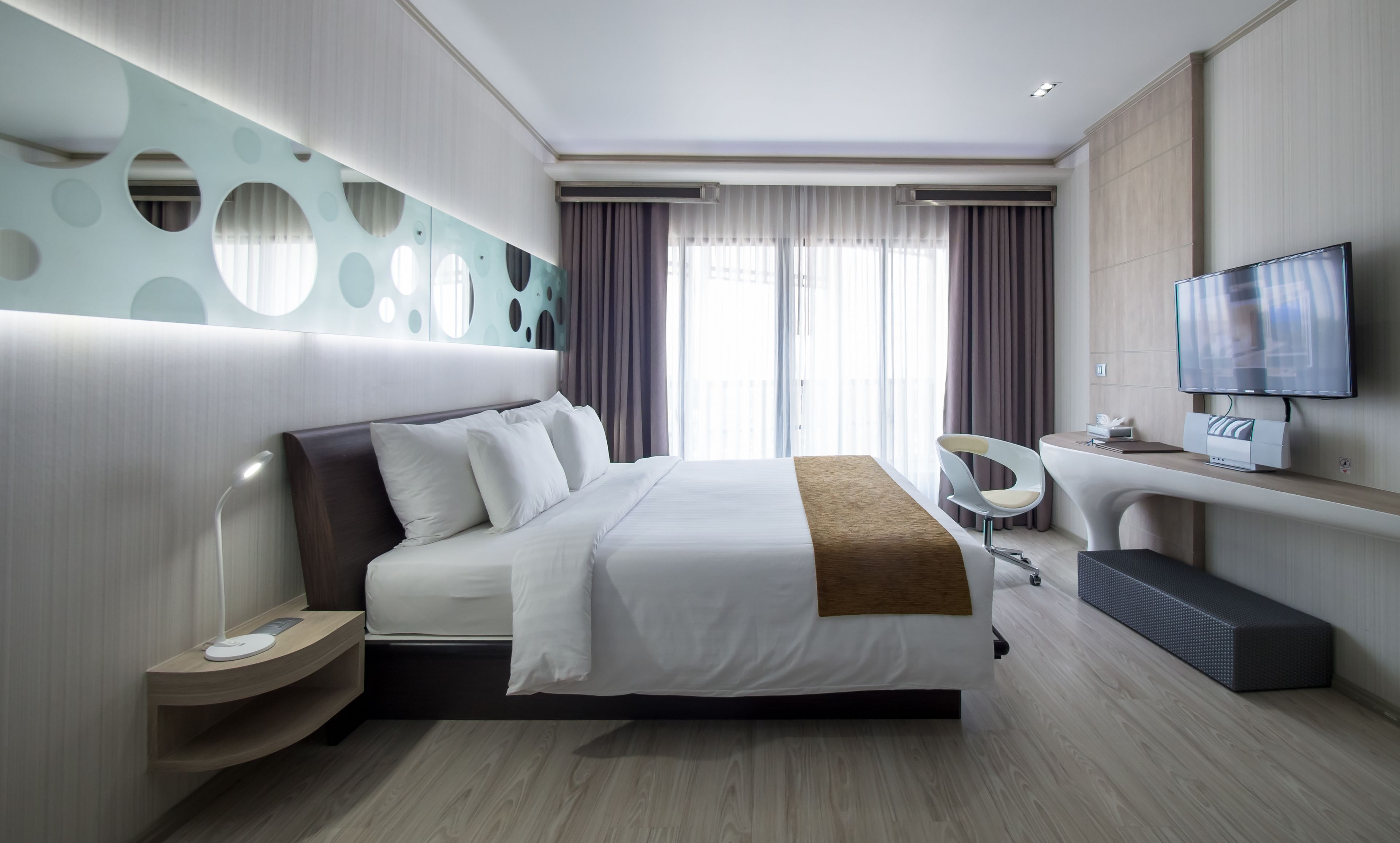 Quarto de hotel moderno com uma cama grande, televisão, secretária e um design de parede único.