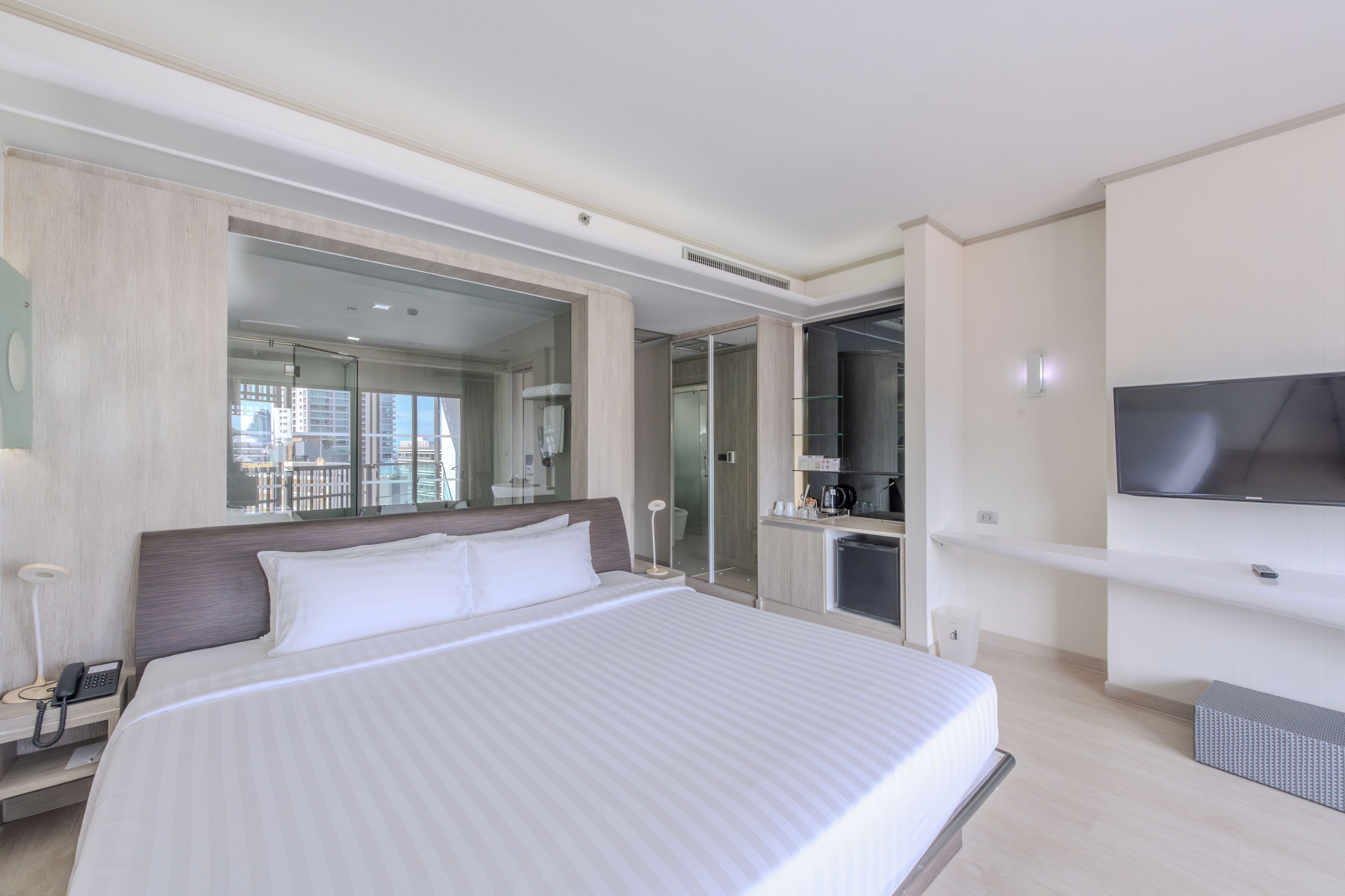 A modern hotel room with a large bed, a television, a minibar, and a bathroom with a glass shower enclosure.