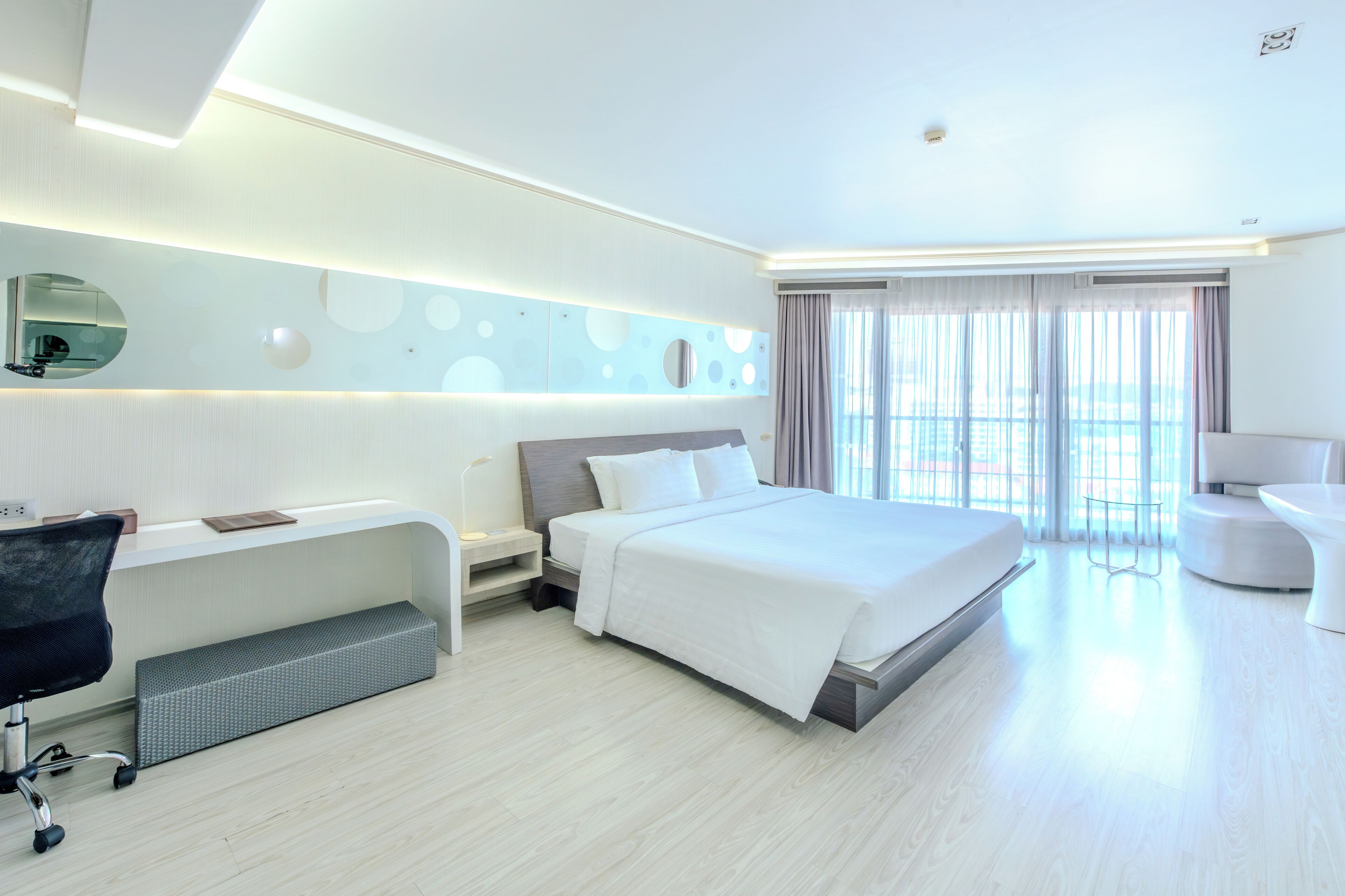 A modern hotel room with a bed, desk, chair, and a large window with curtains.