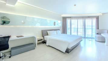 A modern hotel room with a bed, desk, chair, and a large window with curtains.