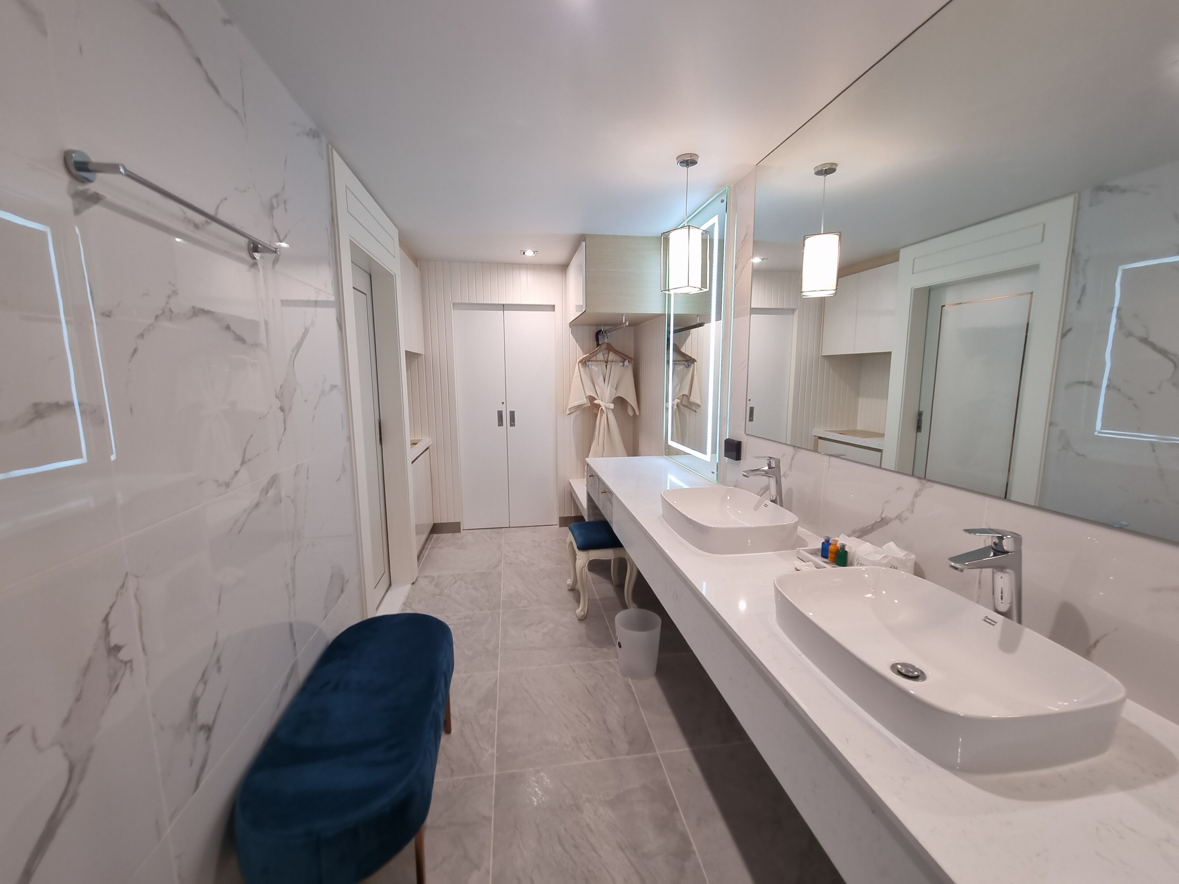 A modern bathroom with a long vanity, two sinks, a large mirror, and marble walls.