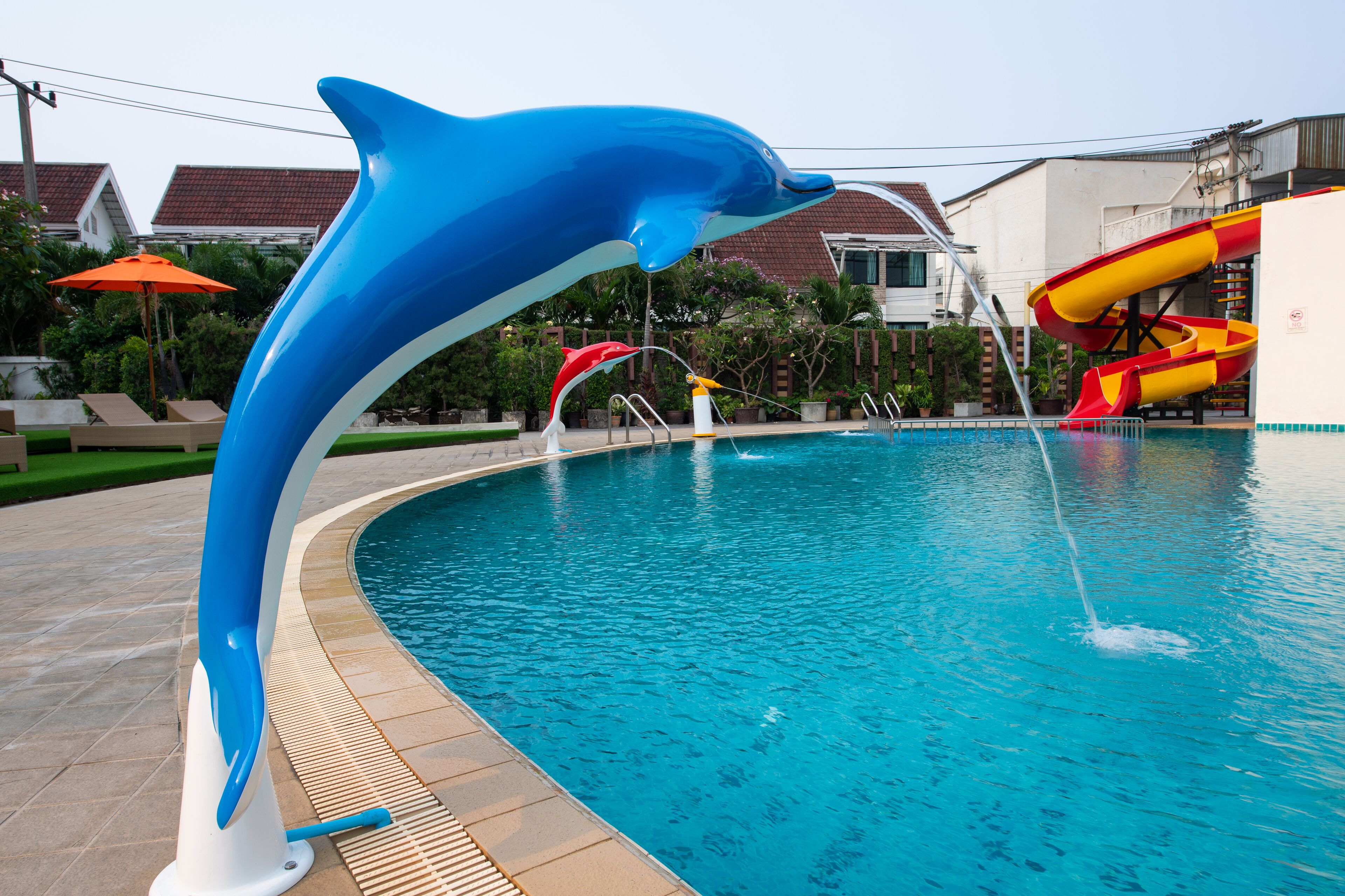 A swimming pool with a dolphin sculpture, a slide, and a lifeguard stand.