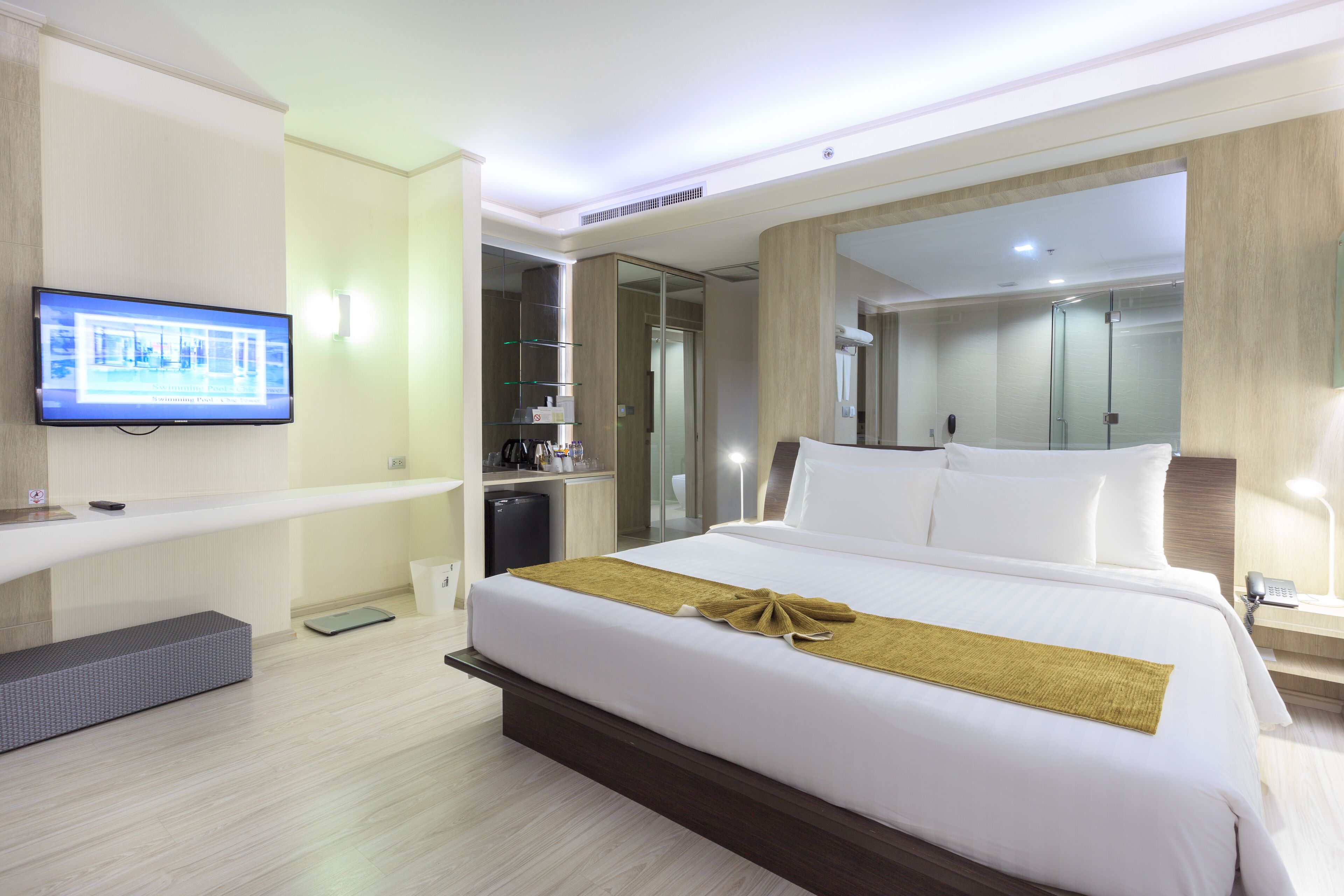 A modern hotel room with a large bed, a television on the wall, a walk-in closet, and a shower area.