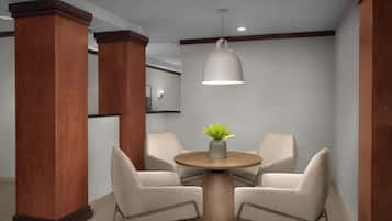 A modern waiting area with two beige chairs around a wooden table, a potted plant, and a pendant light.