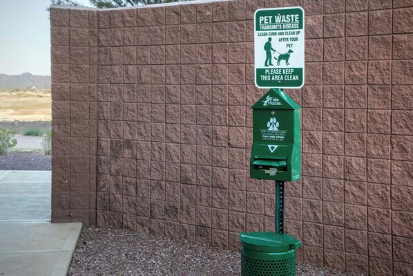 A pet waste disposal station with a sign instructing to clean up after pets and a trash bin. - Fairfield Inn & Suites Phoenix Chandler / Fashion Center (Chandler)