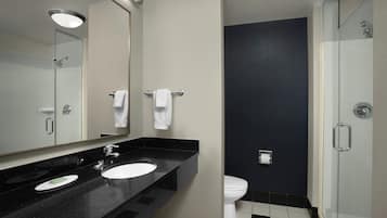A modern bathroom with a black countertop sink, a large mirror, a white toilet, and a glass-enclosed shower.