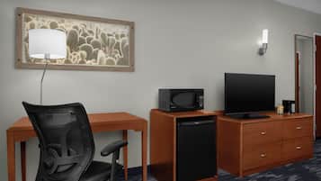 Habitación de hotel con escritorio, silla, televisor, microondas y refrigerador.