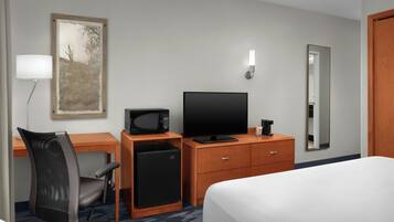 A hotel room with a bed, desk, chair, television, refrigerator, and a mirror.