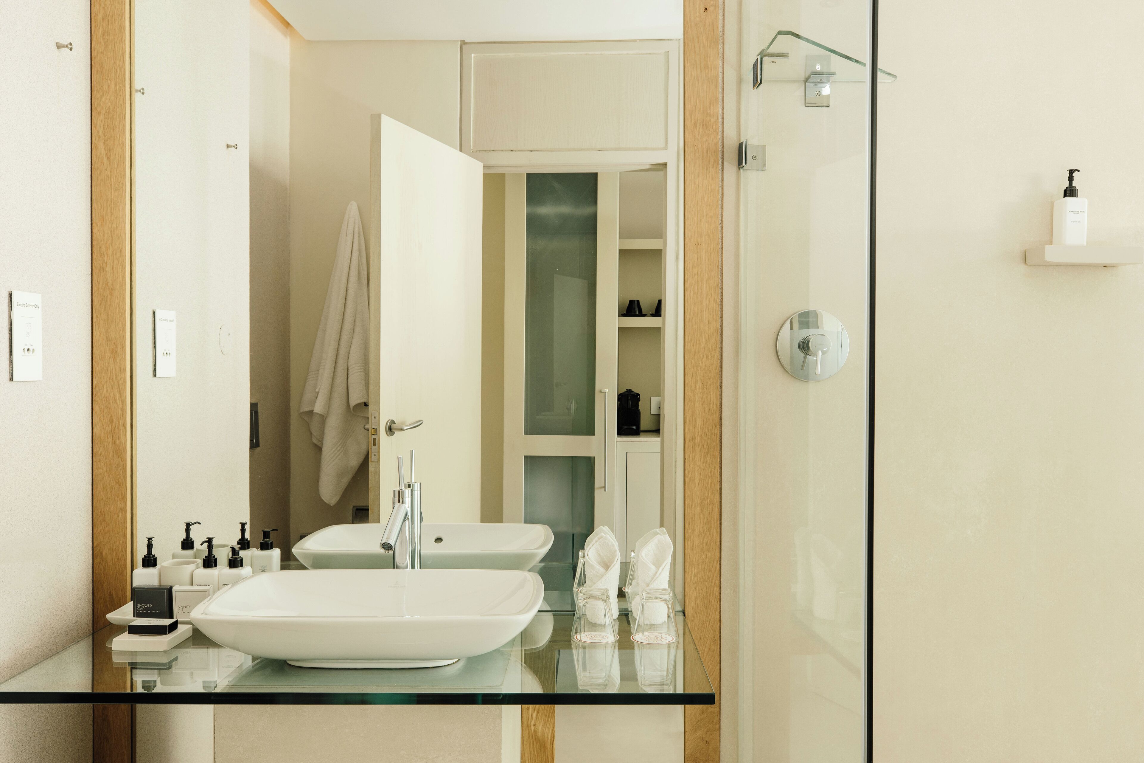 A modern bathroom with two sinks, a glass shower enclosure, and a glass vanity.