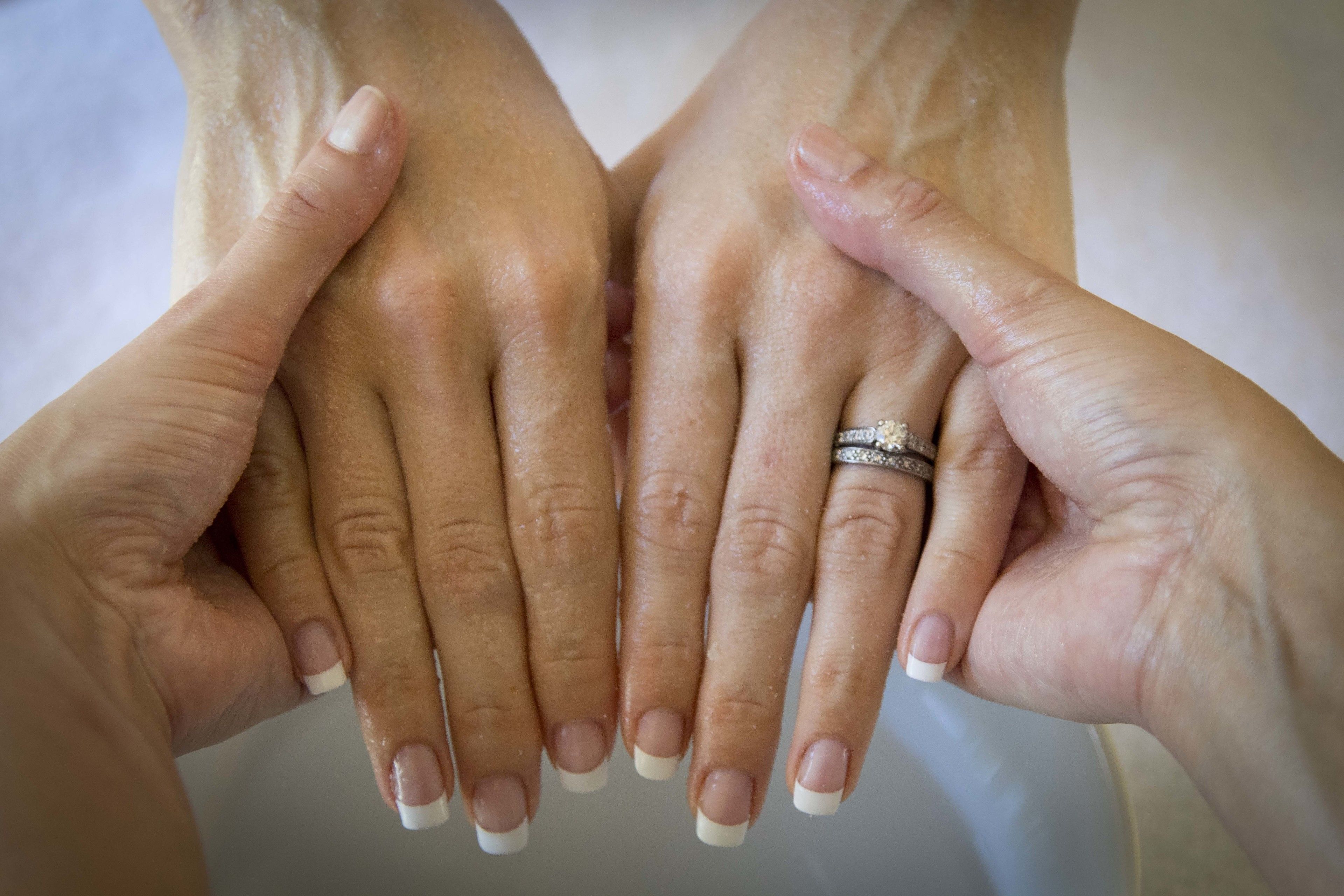 Two hands with French manicure nails and a ring on one finger.