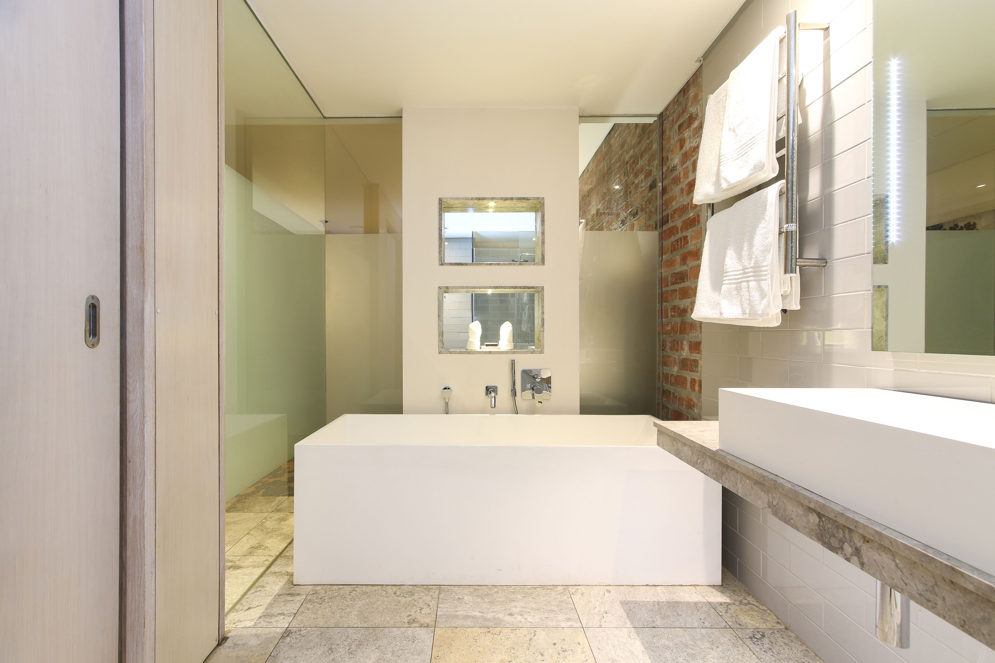 A modern bathroom with a large bathtub, two mirrors, and a white vanity.