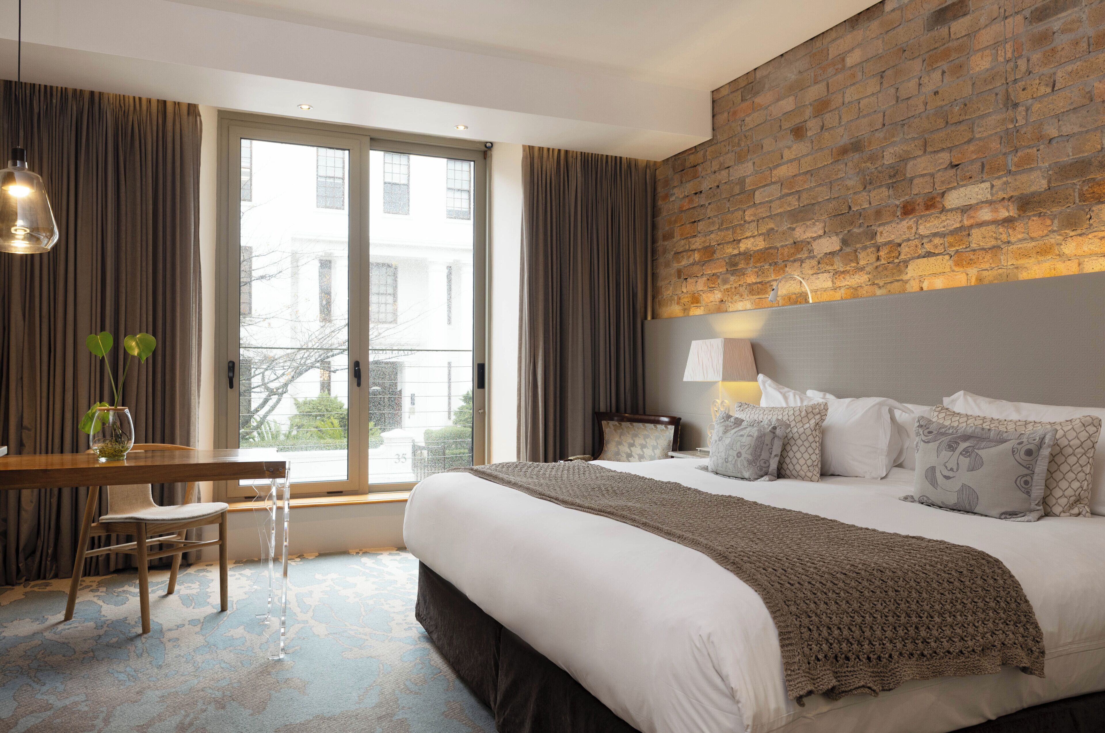 A hotel room with a large bed, a desk, and a view of the city through a large window.