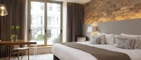A hotel room with a large bed, a desk, and a view of the city through a large window.