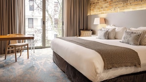 A hotel room with a large bed, a desk, and a view of the city through a glass door. - Oude Werf Hotel (Stellenbosch)