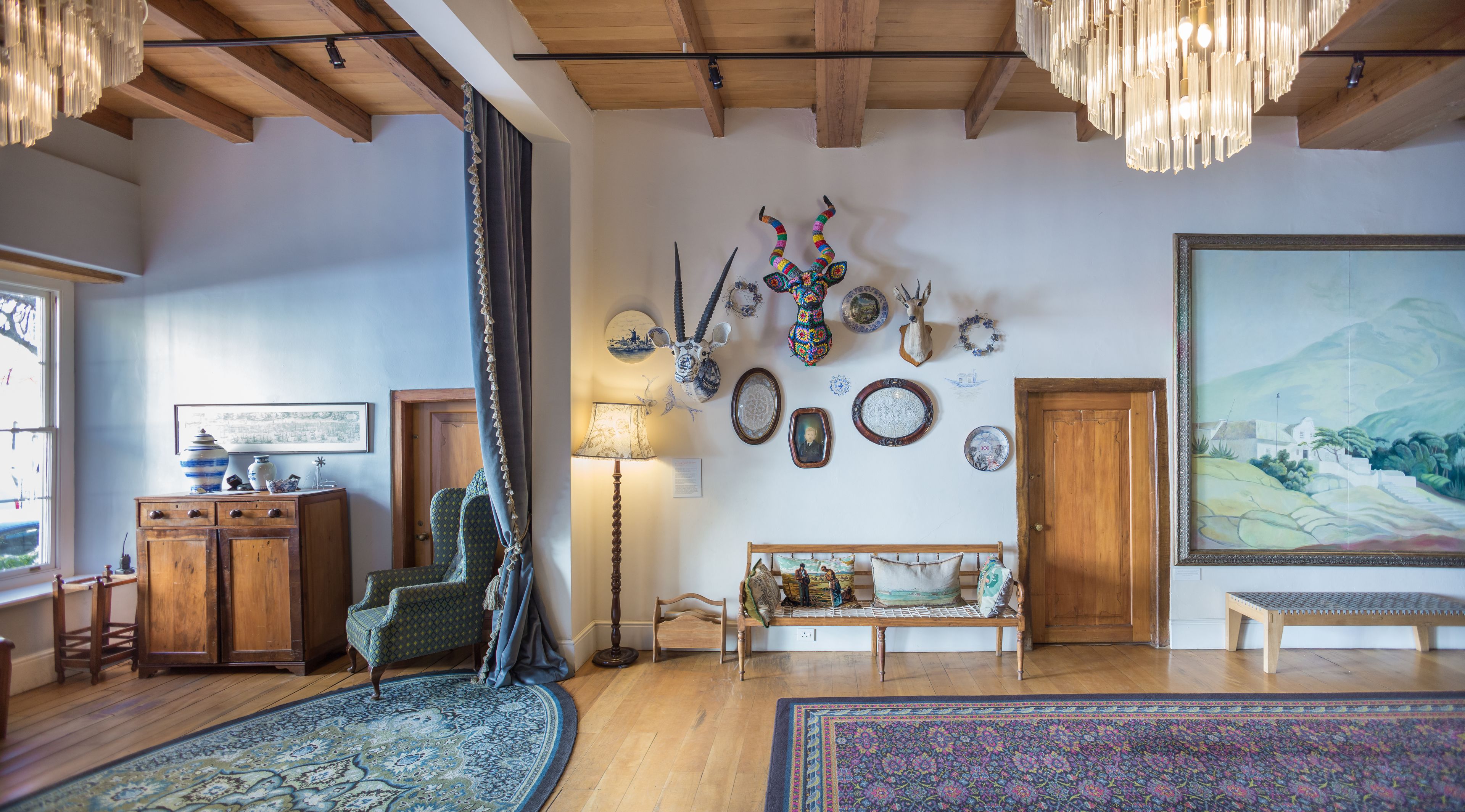 A spacious living room with a high ceiling, wooden beams, a large painting, and various decorative items on the walls.