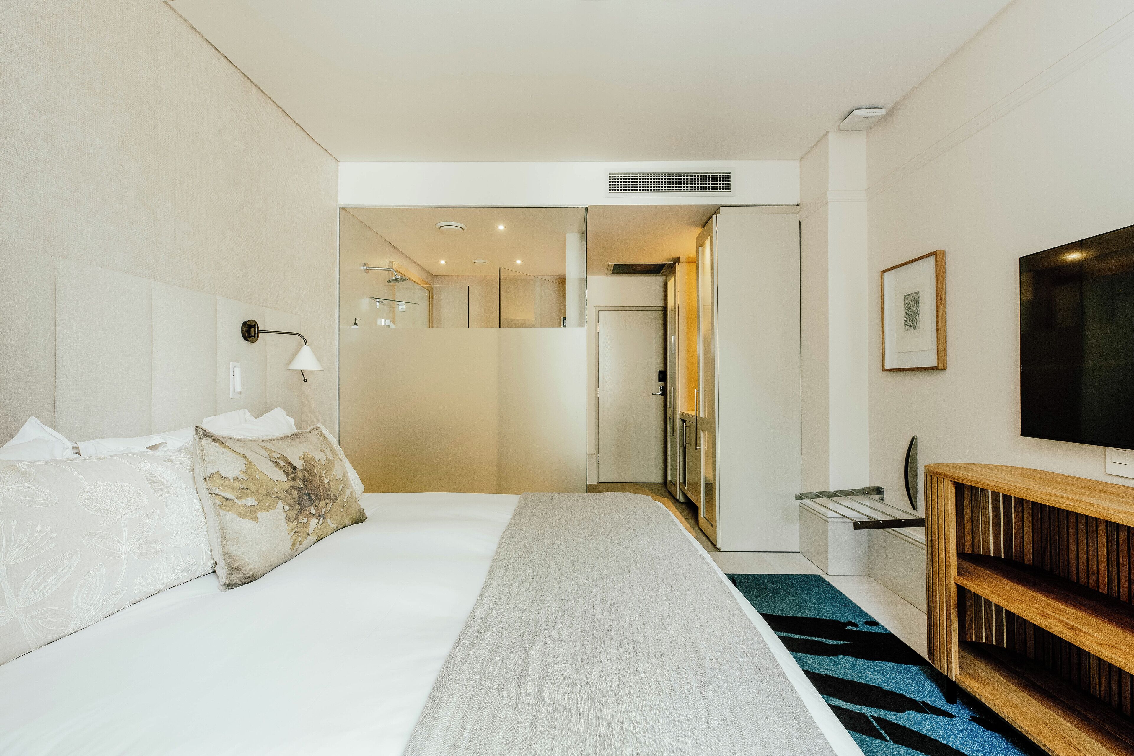 A modern hotel room with a large bed, a wooden console table, a TV, and a bathroom visible through an open door.