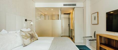 A modern hotel room with a large bed, a wooden console table, a TV, and a bathroom visible through an open door.