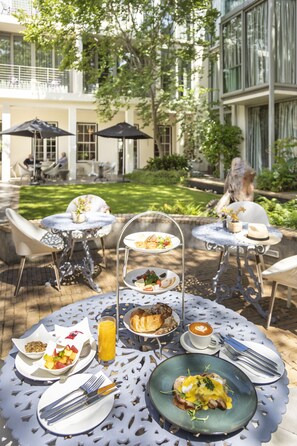 An outdoor dining area with tables, chairs, and a variety of food and drink items. - Oude Werf Hotel (Stellenbosch)