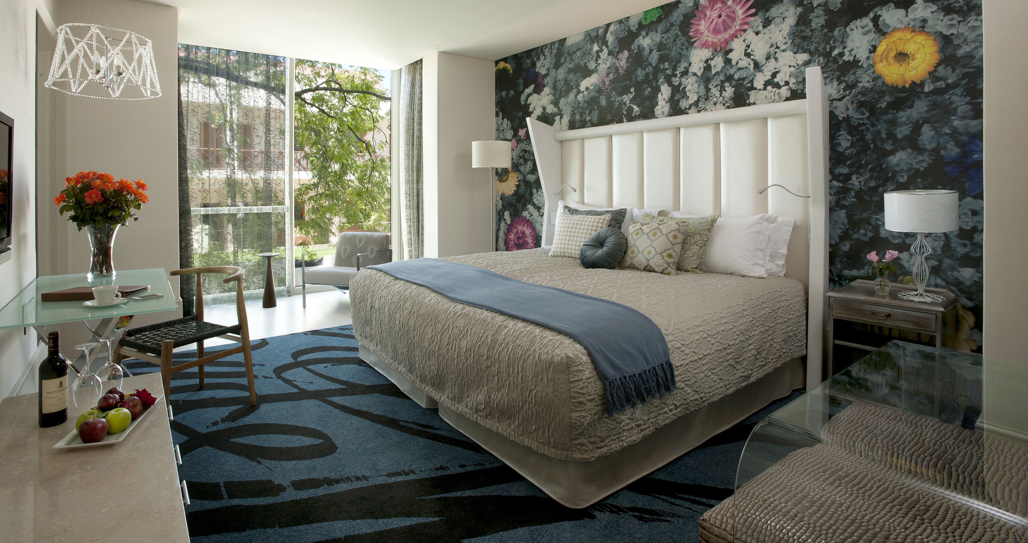 A modern bedroom with a large bed, a glass desk, a chair, and a view of the outdoors.